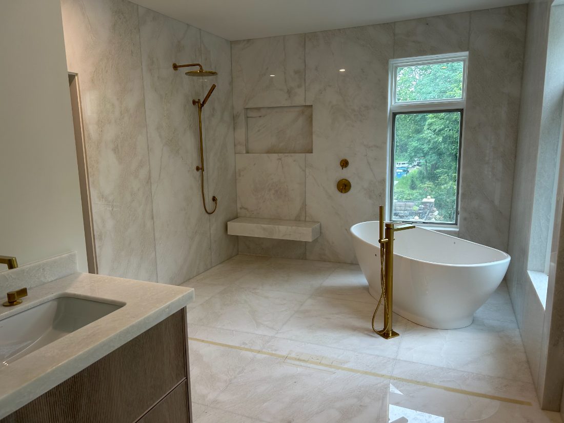 Primary bath with marble slab walls, freestanding tub, and brass fixtures