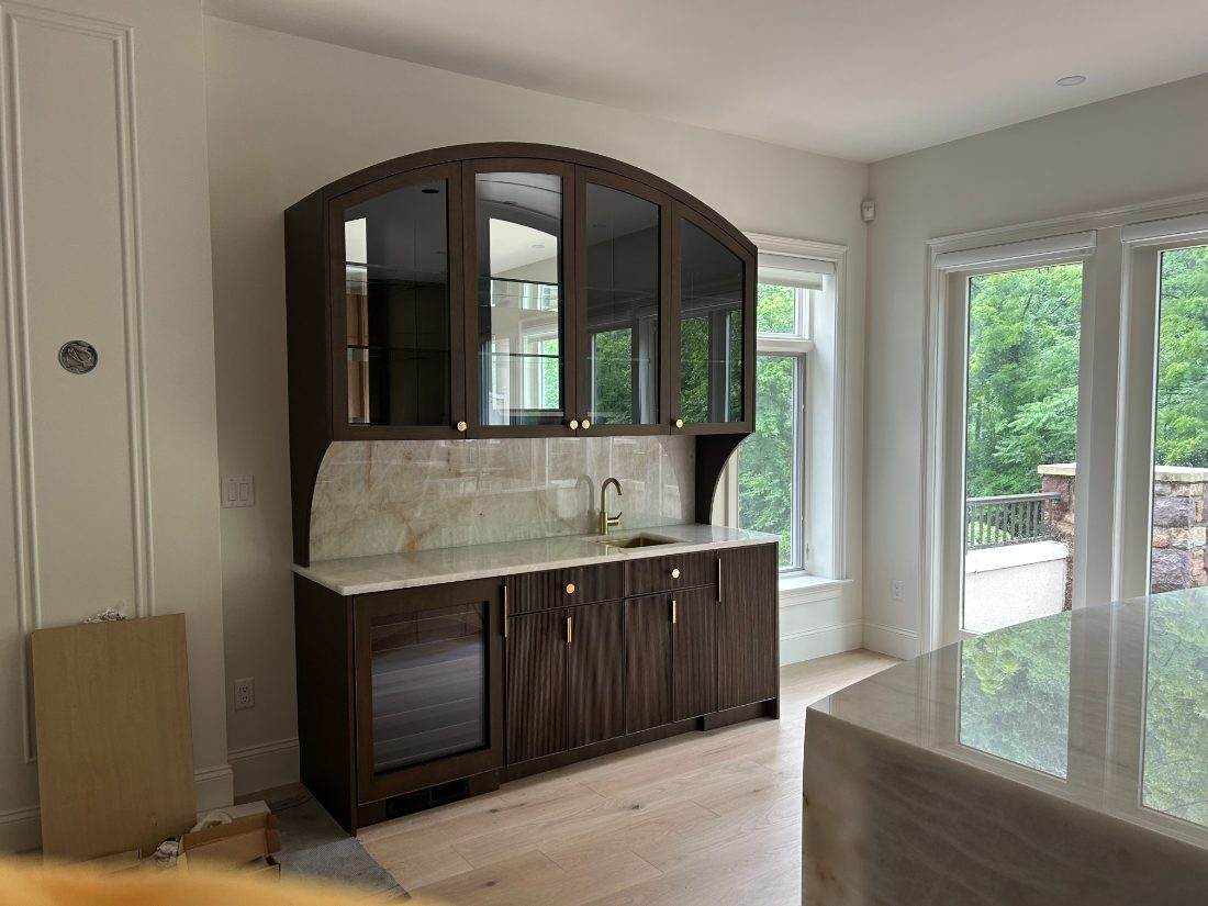 Arched wet-bar built-in with fluted oak cabinetry and quartzite backsplash